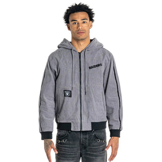 A man wearing a gray zip-up hoodie with black trim, black side stripes, and a black Raiders logo on the chest, paired with dark gray jeans, against a light gray background.