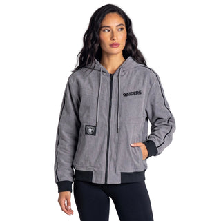 A woman modeling a gray zip-up hoodie jacket with black trim and Oakland Raiders branding, including the team name on the chest and a team logo patch on the pocket, against a plain light gray studio background.