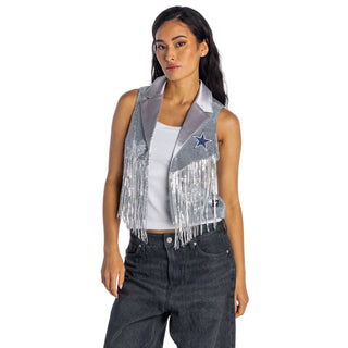 A woman modeling a silver sequined fringed vest with a blue embroidered star on the chest, worn over a white tank top and dark gray jeans against a light gray studio background.